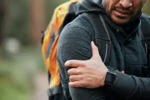 Shoulder pain, injury and person hands with fitness, workout and travel accident from hike. Athlete